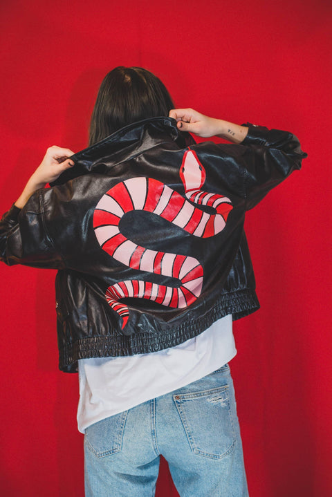 Woman showing a pink and red snake on the back of a black leather jacket.